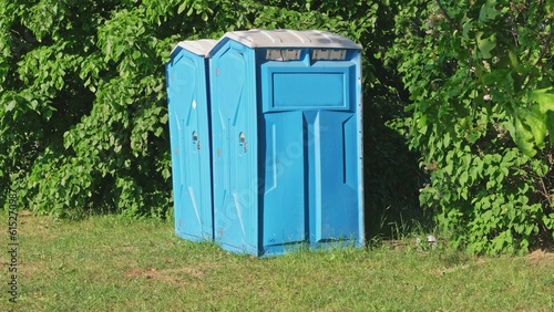 Pair of Blue Plastic Mobile Public Toilet Outhouse Standing in the Middle of High Grass Meadow During Open Air Event Music Festival