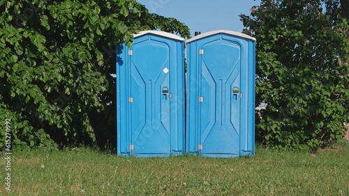 Pair of Blue Plastic Mobile Public Toilet Outhouse Standing in the Middle of High Grass Meadow During Open Air Event Music Festival
