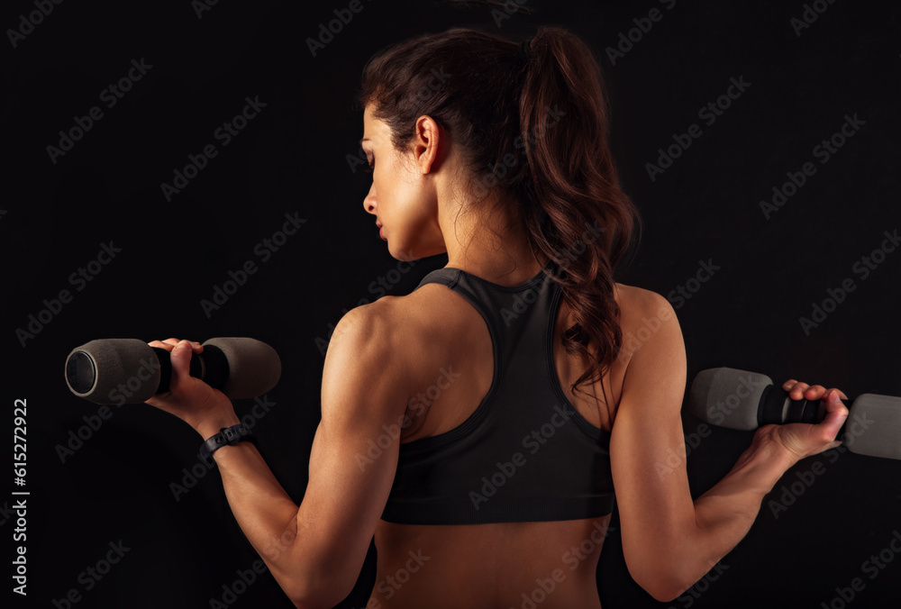 Female sporty muscular young serious woman doing strength workout on the shoulders, biceps and arms in sport bra holding dumbbells on black background. Closeup Female sporty muscular young serious woman doing strength workout on the shoulders, biceps and arms in sport bra holding dumbbells on black background. Closeup