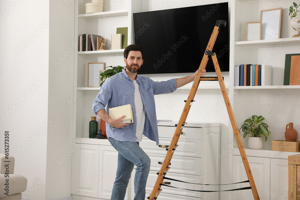 Man with books on wooden folding ladder at home
