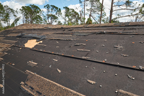 Damaged house roof with missing shingles after hurricane Ian in Florida. Consequences of natural disaster