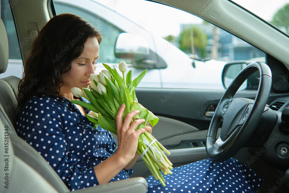 Young stylish woman driver sitting behind steering wheel of her car holding a bouquet of flowers