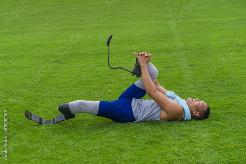 Asian athlete with prosthetics stretches on grass lawn, concluding his speed running practice at the stadium