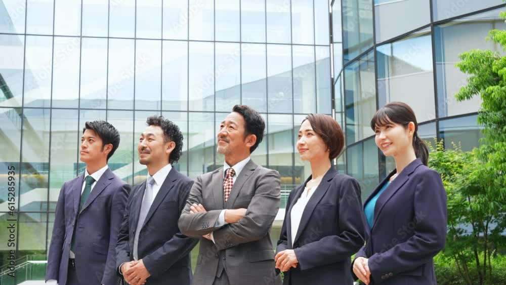 A group of business people of various generations lined up in front of an office building with smiles. A group of business people of various generations lined up in front of an office building with smiles.