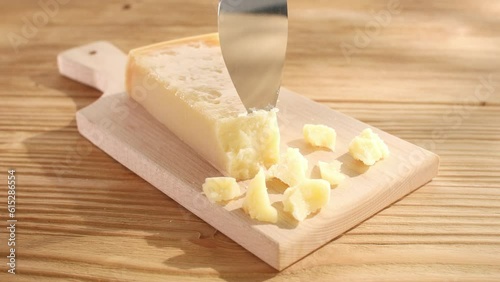 Hard cheese is chipped off with a knife on a cutting board. Wooden background. Parmesan with broken pieces. Traditional Italian cheese grana parmigiano reggiano. Close-up. High quality 4k footage