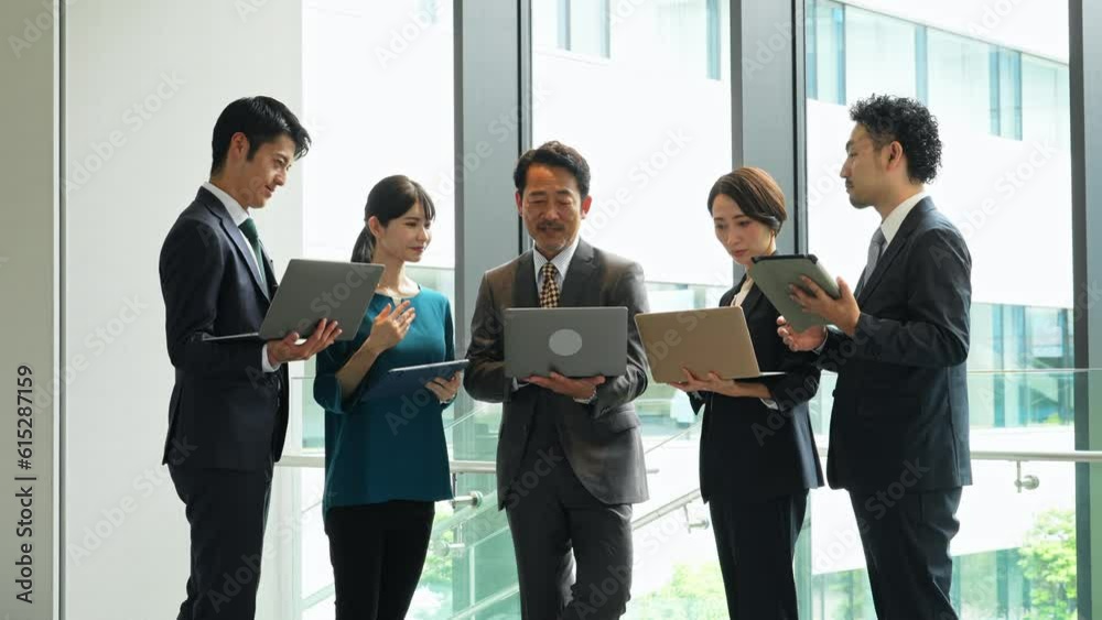 Group of Asian businesspeople meeting in lobby with laptops and tablets. Digital transformation. Smart office.