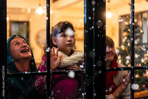Adorable child looking at the window and first snow flakes with family.  © Kawee