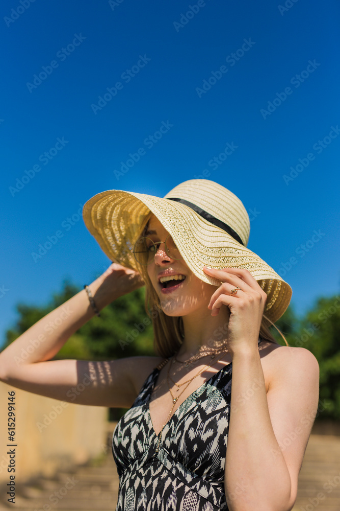 Happy woman with hat smiling and laughing standing outside at the beach on a sunny day