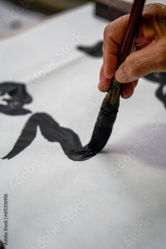 An old Chinese calligrapher is writing brush characters, creating Chinese calligraphy works. Translation: Spring comes, the god of wind arrives.