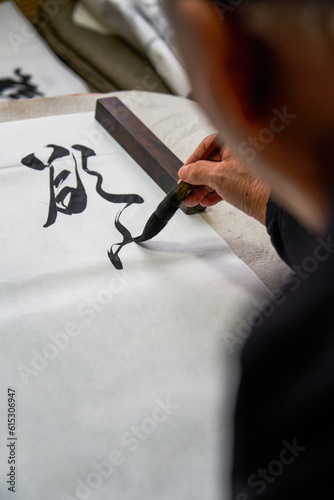 An old Chinese calligrapher is writing brush characters, creating Chinese calligraphy works.
Translation: Spring comes, the god of wind arrives.