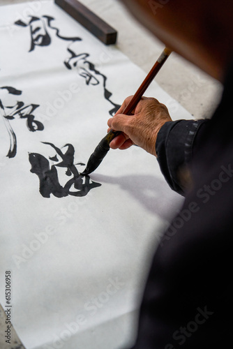 An old Chinese calligrapher is writing brush characters, creating Chinese calligraphy works.
Translation: Spring comes, the god of wind arrives. photo
