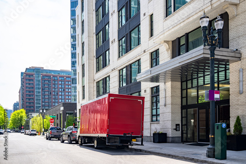 Fototapeta Naklejka Na Ścianę i Meble -  Compact small rig semi truck with red box trailer making customer delivery standing on the urban city street with multilevel apartment buildings