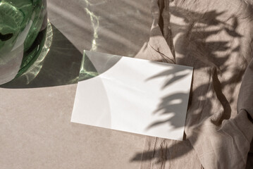 Blank paper card mock up on beige tabletop background with aesthetic sunlight shadows, minimalist business brand template, wedding invivation design, copy space