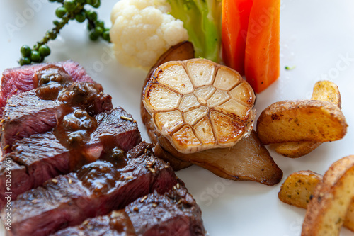 The close-up photograph captures a piece of grilled garlic nestled in a plate of beef steak photo