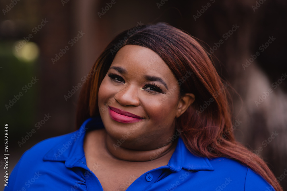Smiling confidently at the camera, a young African American woman with auburn hair poses in a blue dress for a portrait. Smiling confidently at the camera, a young African American woman with auburn hair poses in a blue dress for a portrait.