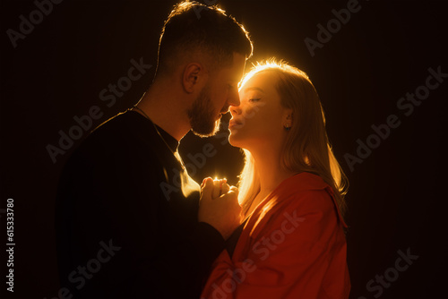 Canvastavla Side view of young bearded man and blond haired woman holding hands and kissing gently in darkness against glowing warm light