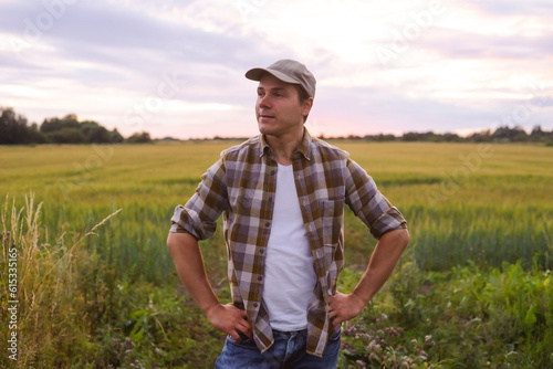 Farmer in front of a sunset agricultural landscape. Man in a countryside field. Country life, food production, farming and country lifestyle concept.