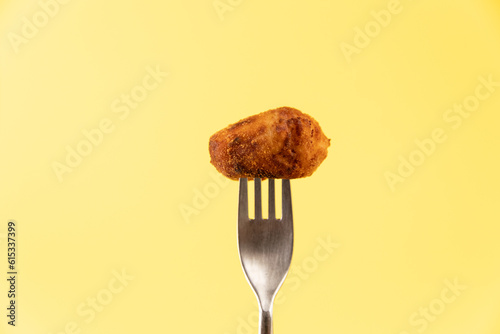 Homemade traditional spanish croquette on a fork on yellow background isolated photo