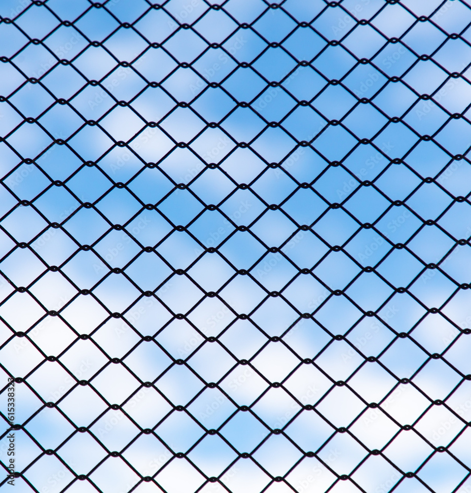 Chain link fence against the blue sky and clouds. Abstract background Chain link fence against the blue sky and clouds. Abstract background