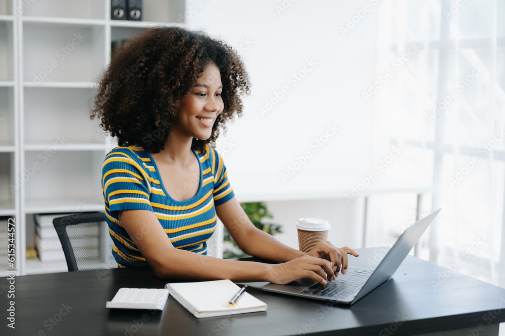 Beautiful African woman using laptop and tablet while sitting at her working place. Concentrated at work in home office Beautiful African woman using laptop and tablet while sitting at her working place. Concentrated at work in home office