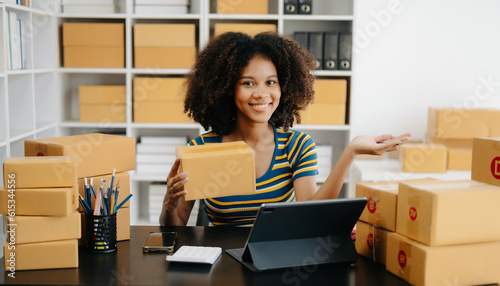 Startup small business SME, Entrepreneur owner African woman using smartphone or tablet taking receive and checking online purchase shopping order to preparing pack product box. .