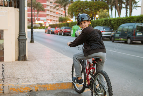 a child of European appearance rides a bicycle, wearing a black helmet in casual clothes, along the city street. Close-up on a boy, there is a place for an inscription