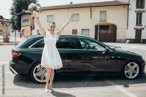 Adult woman in front of the bride and groom's car raising her hands happily before the wedding and waving with a bouquet of colorful flowers in her hand