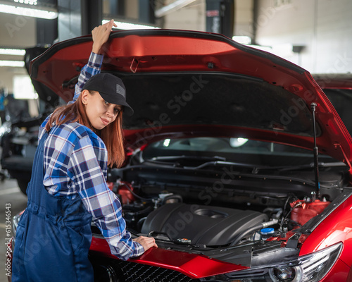 Woman auto mechanic opens the hood of a car in a car service. 