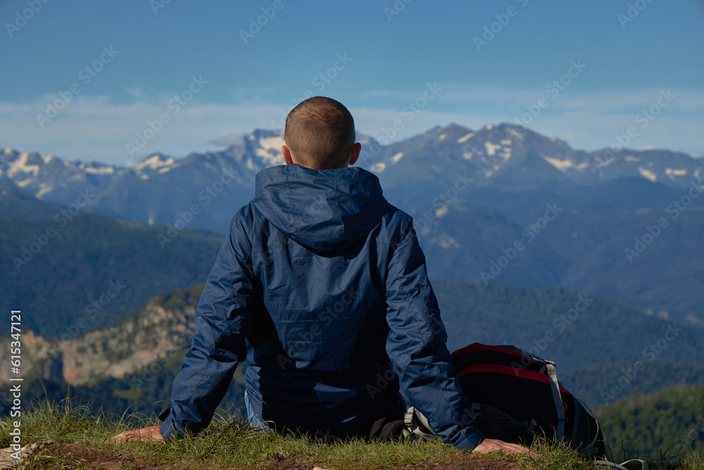 man with backpack on top of a hill with mountains, landscape. man sitting on grass overlooking mountains man with backpack on top of a hill with mountains, landscape. man sitting on grass overlooking mountains