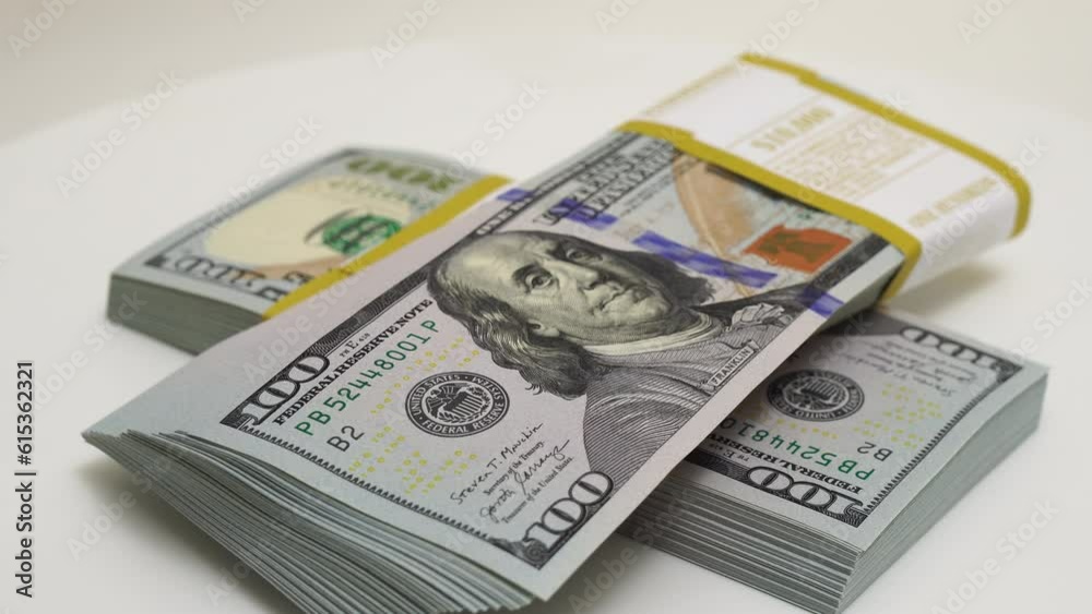 stack of bank bundles with US dollars on a white background. Close-up shot of new, freshly printed hundred-dollar bills rotating on a table. cash flow, business investment, or big money concepts. stack of bank bundles with US dollars on a white background. Close-up shot of new, freshly printed hundred-dollar bills rotating on a table. cash flow, business investment, or big money concepts.