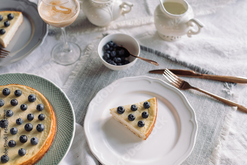 Homemade cheesecake with blueberries on top. Table setting for coffee and tea. 