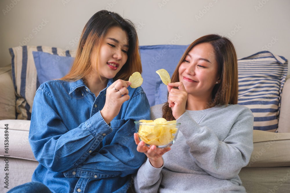 Portrait image of a young couple women sharing and eating potato chips together Portrait image of a young couple women sharing and eating potato chips together