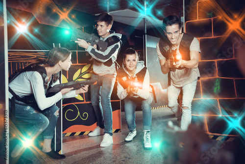 Modern pleasant positive young people with laser pistols playing laser tag on dark labyrinth
