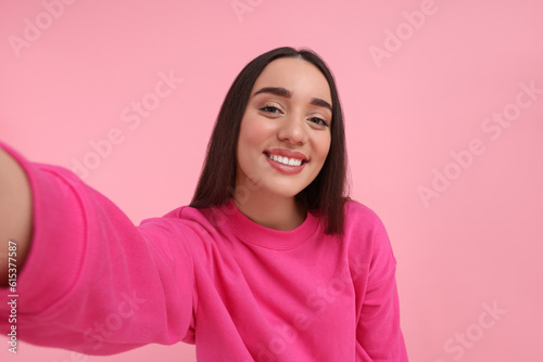 Konstfotografi Smiling young woman taking selfie on pink background