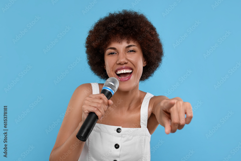 Curly young woman with microphone singing on light blue background Curly young woman with microphone singing on light blue background
