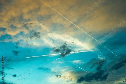 Beautiful poetic photo of a sky with clouds at sunset dusk with nice pastel yellow blue and pink colors, with airplane contrails 