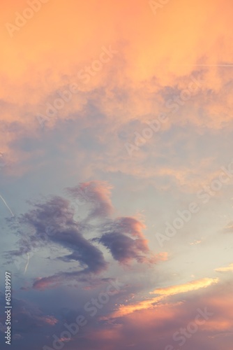 Beautiful poetic sot of a sky with clouds at sunset dusk with nice pastel yellow blue and pink colors, with airplane contrail 