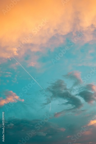 Beautiful poetic picture of a sky with clouds at sunset dusk with nice pastel yellow blue and pink colors, with airplane contrail 
