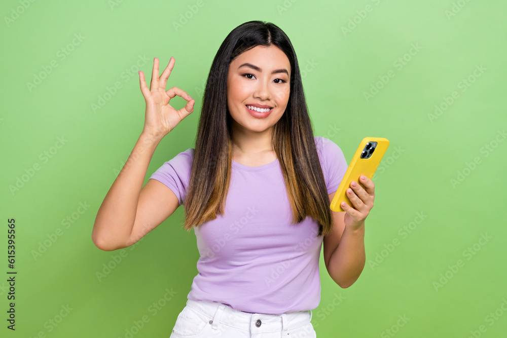 Photo of lovely young vietnamese chinese lady show okey sign gadget dressed stylish violet garment isolated on green color background Photo of lovely young vietnamese chinese lady show okey sign gadget dressed stylish violet garment isolated on green color background