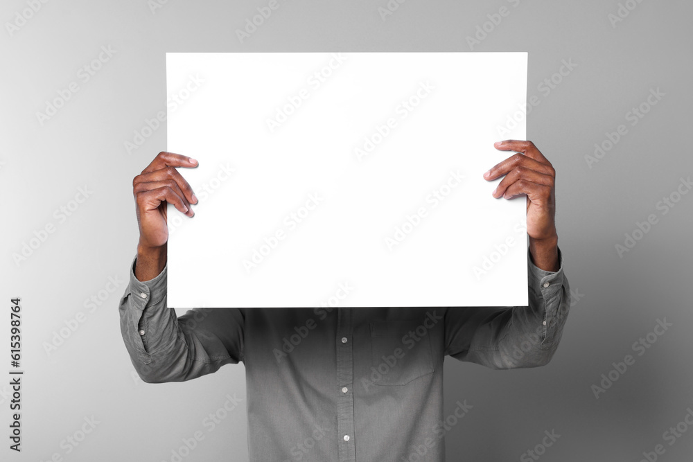 African American man holding sheet of paper on grey background. Mockup for design African American man holding sheet of paper on grey background. Mockup for design