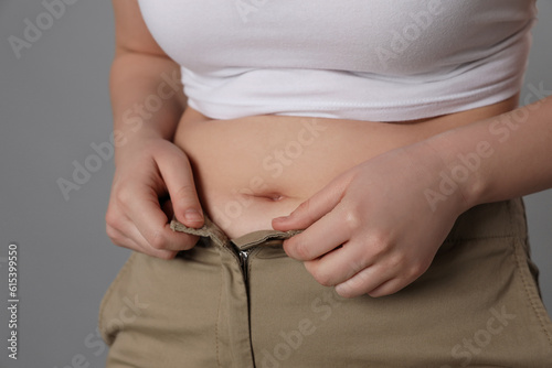Overweight woman trying to button up tight pants on grey background, closeup
