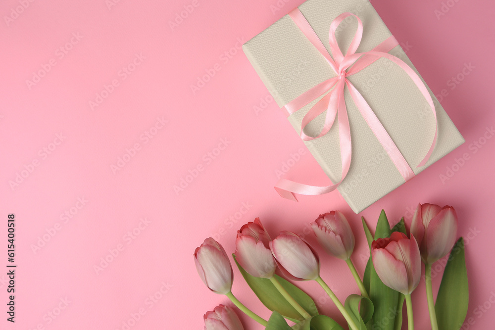 Beautiful gift box with bow and tulips on pink background, flat lay. Space for text