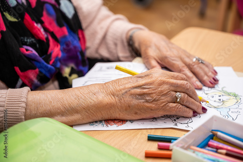 Elderly woman painting color on her drawing. Hobby at nursing home. High quality photo