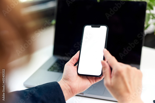 A brunette woman holding a mobile phone typing on a blank white screen. © bnenin