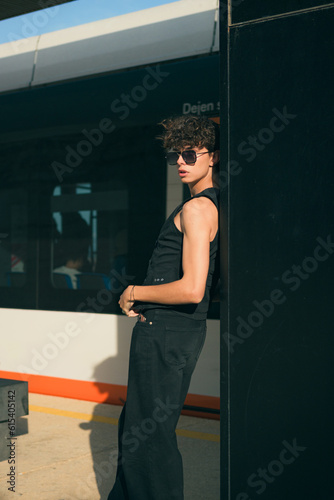 Young alternative man in black clothes posing in a station at sunset