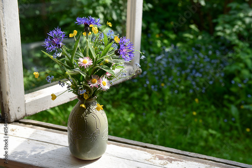 Bouquet of wild flowers in a vase on a wooden window sill. Floral decoration on the window of an old country house, summer cottage. Country life aesthetics