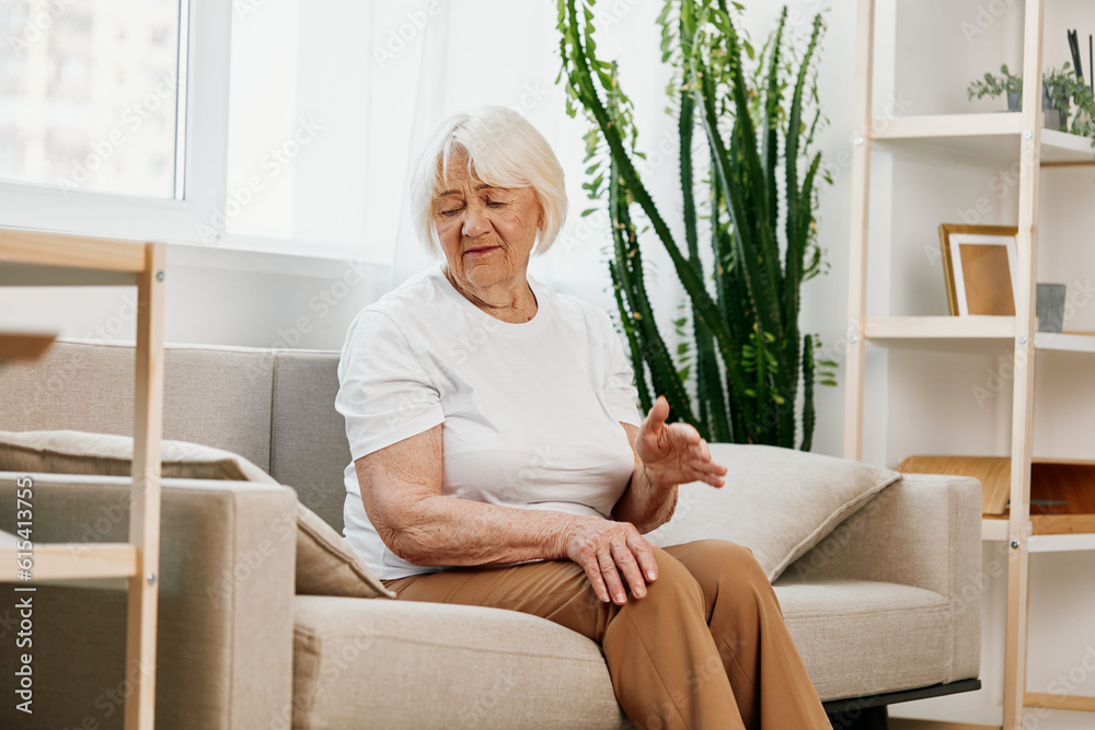 Elderly woman severe pain in her leg sitting on the couch, health problems in old age, poor quality of life. Grandmother with gray hair holds on to her sore knee, problems with joints and ligaments Elderly woman severe pain in her leg sitting on the couch, health problems in old age, poor quality of life. Grandmother with gray hair holds on to her sore knee, problems with joints and ligaments