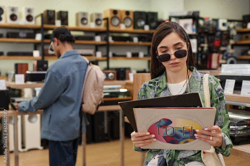 Obraz premium Waist up portrait of young woman holding set of vinyl records in music store, copy space