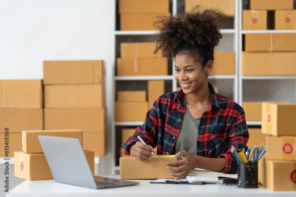 African american young woman startup business concept ecommerce business owner online on laptop Work on packing products, parcel boxes, recording customer address information for packaging delivery. African american young woman startup business concept ecommerce business owner online on laptop Work on packing products, parcel boxes, recording customer address information for packaging delivery.