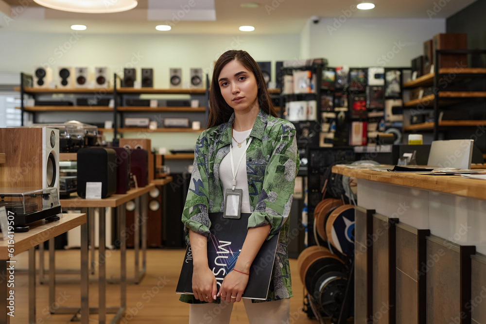 Portrait of young woman working in music store amd holding vinyl record looking at camera, copy space